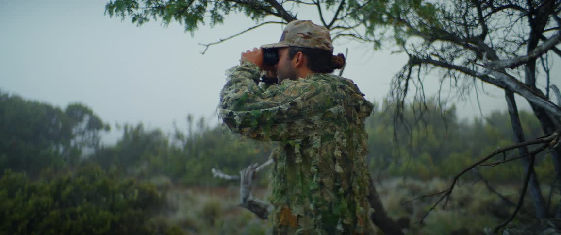 The man is using binoculars on the field