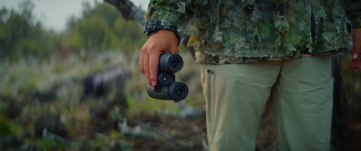 A hunter in camouflage clothing holds a pair of binoculars in his hand the video shows a closeup of his hand and the binoculars