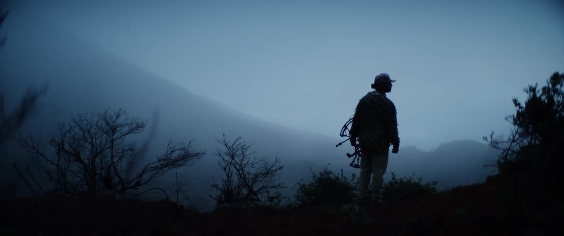 Silhouetted person holding equipment at dusk in the misty mountains