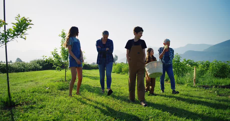 A family walk across a grassy field on a farm together as they smile and laugh on a sunny day