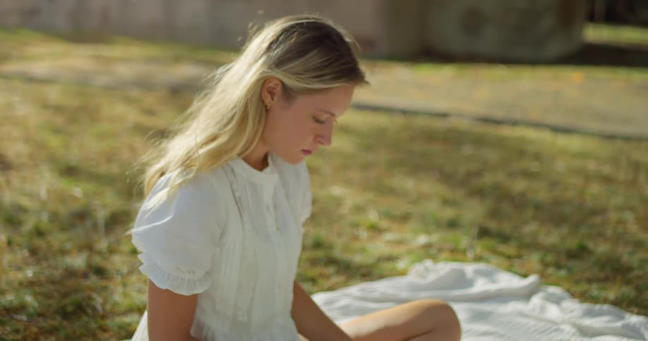 Female in a white dress sitting on a white blanket on the grass reading a book