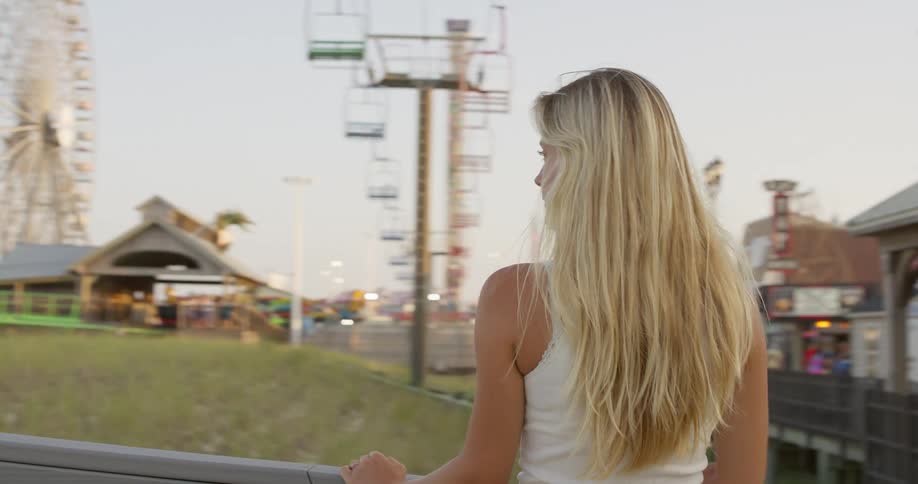 Woman looks at amusement park with roller coaster and ferris wheel