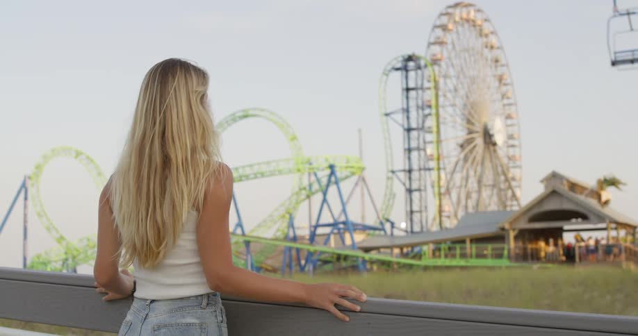 Woman watching a roller coaster and ferris wheel at an amusement park