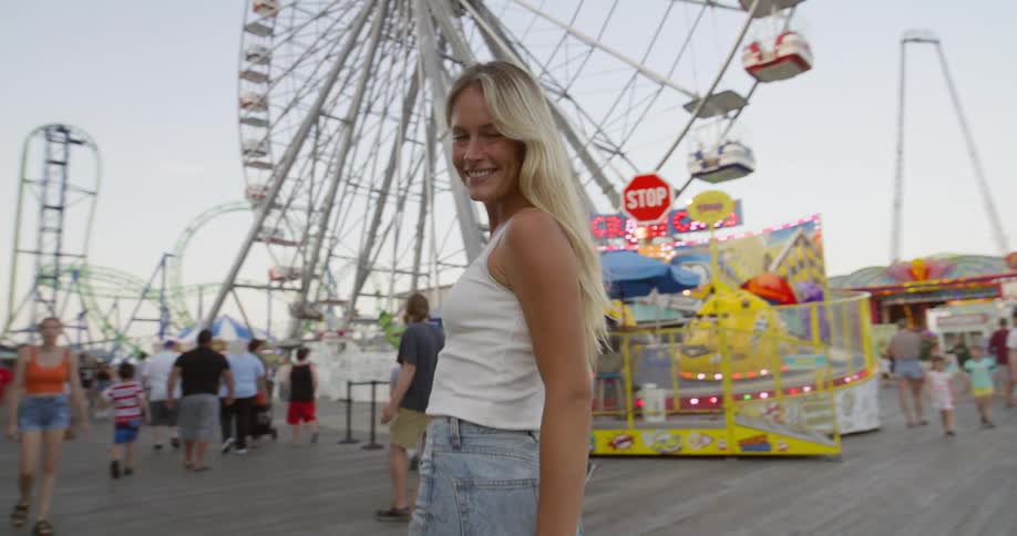 Blonde female walking towards ferris wheel turns and smiles