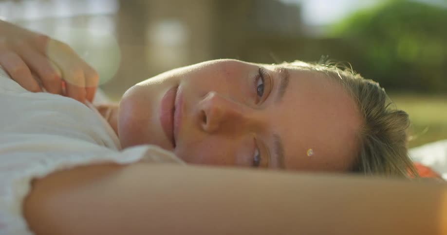 A woman lies outdoors smiling warmly in soft natural light