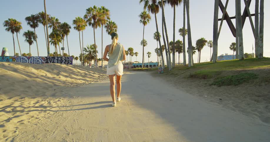 Woman walks along a boardwalk surrounded by palm trees on a sunny day