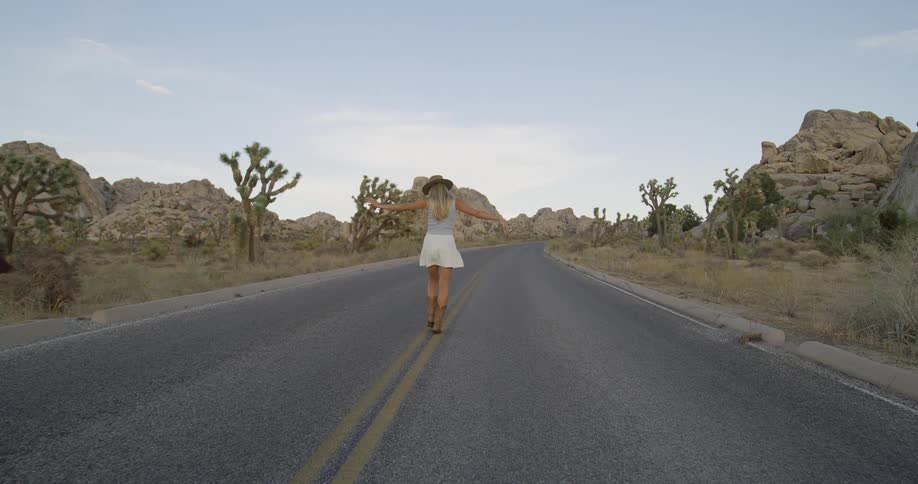 Woman walking in the middle of the empty road between trees and rocks