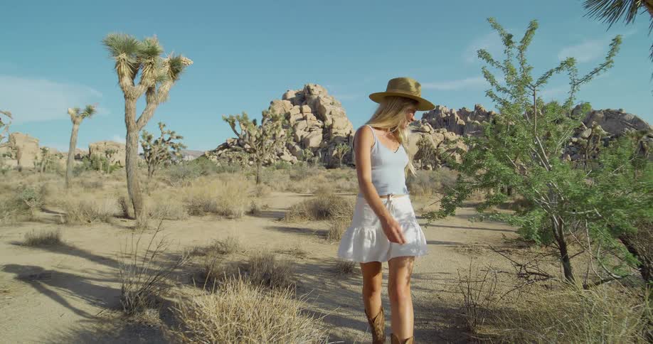 A woman in a hat and boots smiles as she walks through a desert area