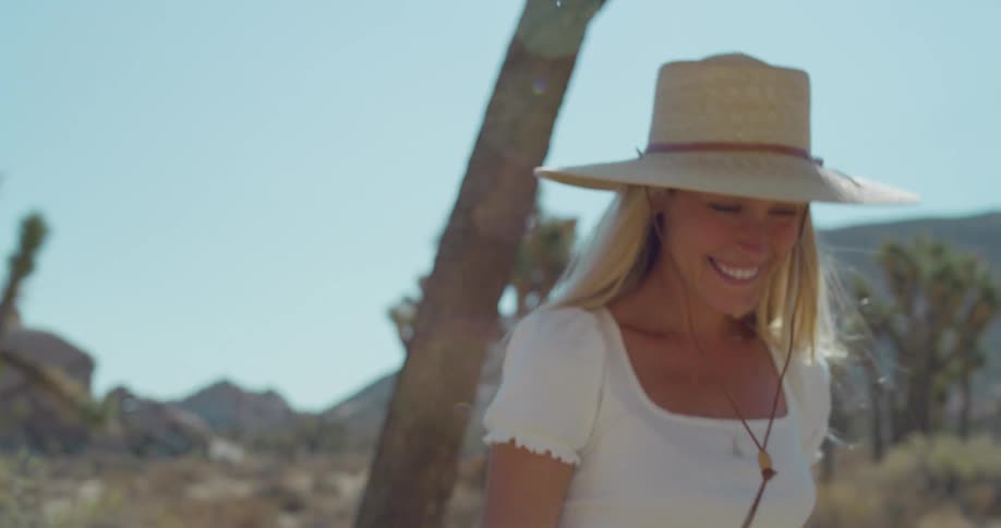 A young woman wearing a hat walks on land smiling under the sun
