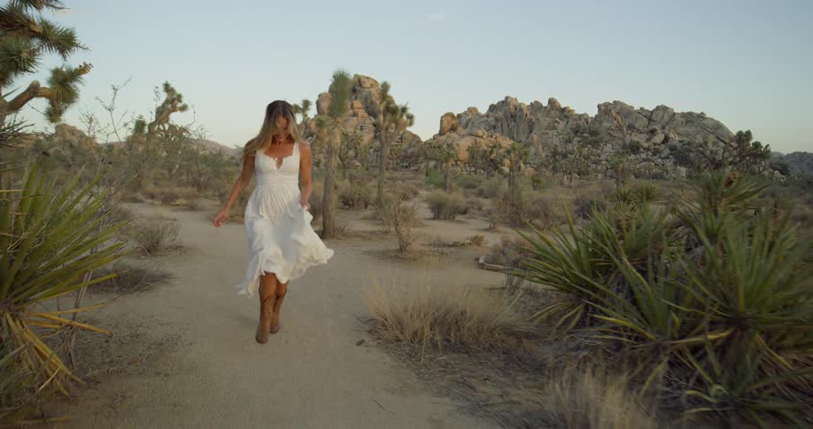 Happy woman in a white dress and cowboy boots running through the desert