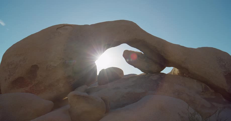 The video shows a natural rock arch formation with the sun shining through it the camera is positioned low with the suns rays creating a bright halo effect around the rocks the watermark filmsupply is visible on the video