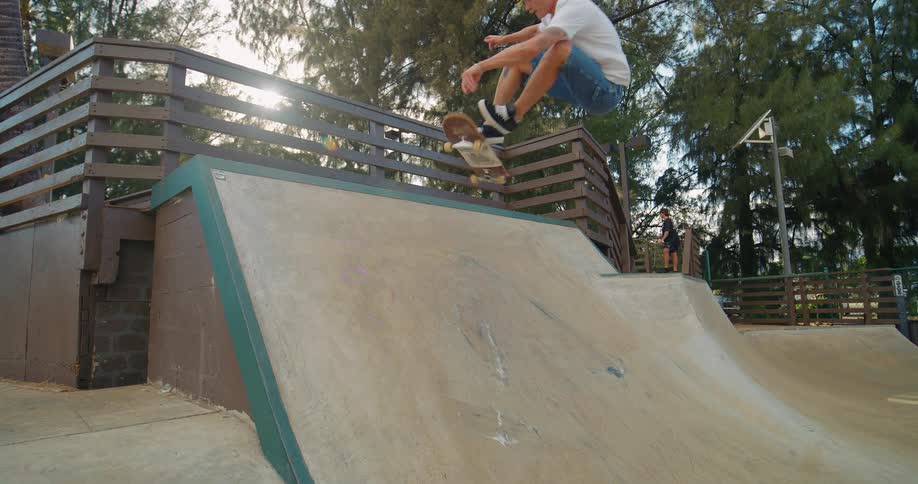 A teenage boy on a skateboard jumps off a ramp at a skate park he lands back on the ramp and then skates away