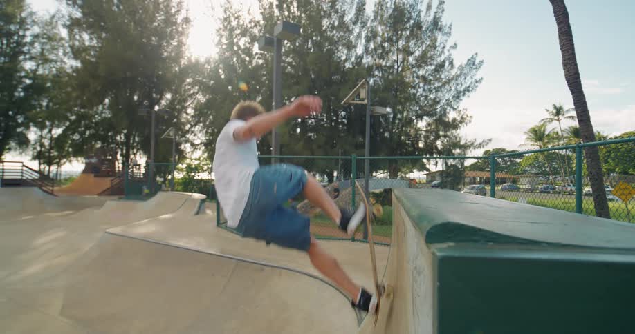The video shows a lowangle shot of a male skateboarder at a skatepark dressed in a white tshirt and blue shorts he performs a grinding maneuver on the edge of a curved concrete ramp before rolling away
