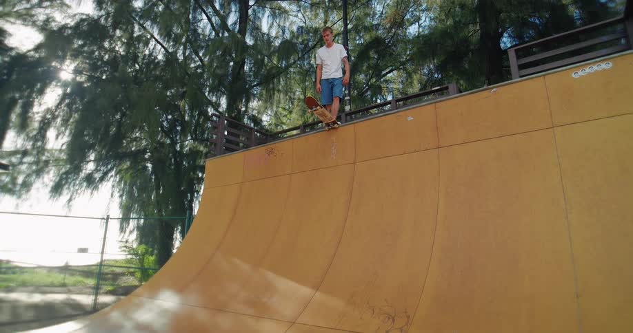 A rider drops into a smooth wooden ramp knees bent and focused framed by towering trees for a dynamic energetic feel