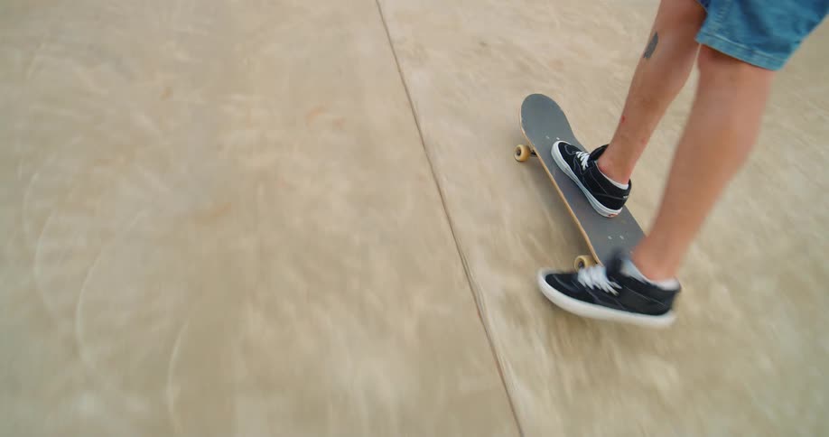 The video shows a person wearing denim shorts and black and white shoes performing a skateboarding trick they are riding a skateboard in a skate park with a concrete ramp