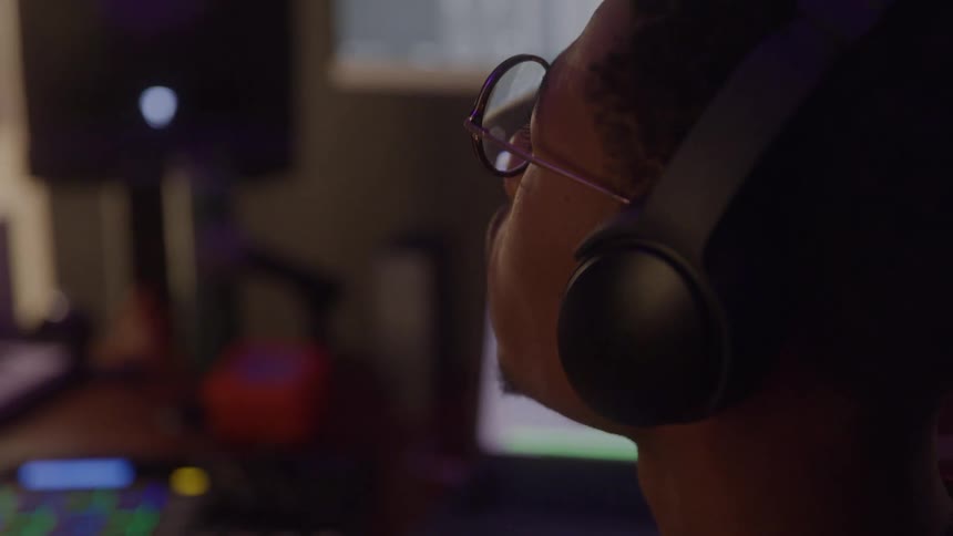 Man with glasses and headphones works at desk with colorful audio equipment