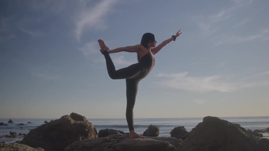A woman practices yoga on coastal rocks at sunrise