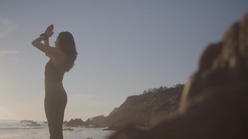 Woman in prayer position on the beach at sunset
