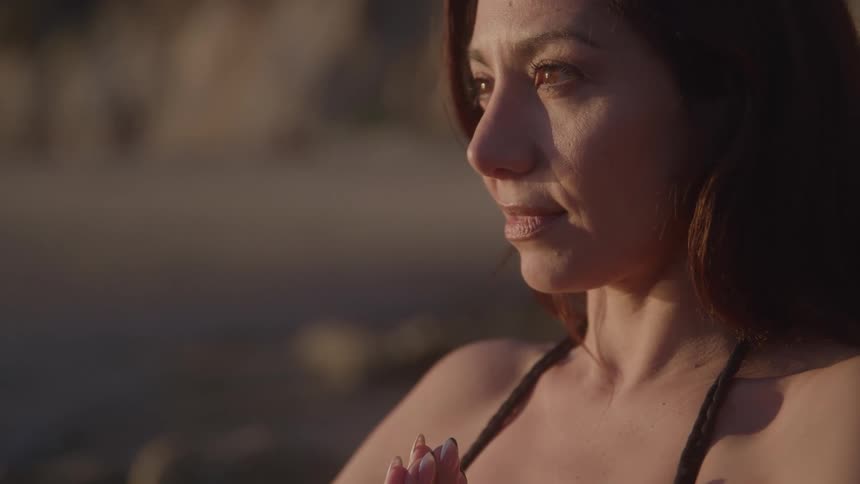 Woman in meditation pose with hands together at sunset
