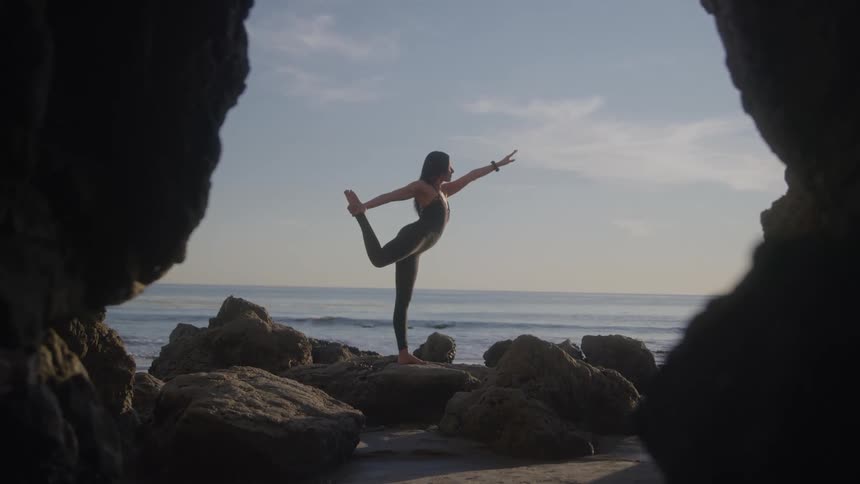 A woman practices yoga on rocky cliffs by the ocean