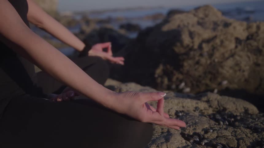 Hands in meditation pose on the rocks by the sea