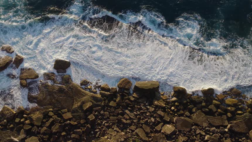 The water crashes against the rocks of the shore