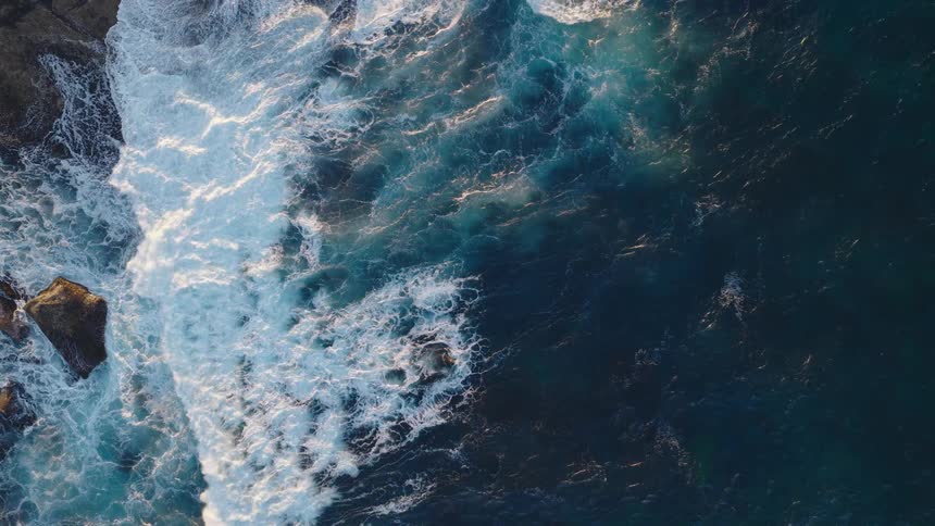 Waves crash against the rocks seen from above