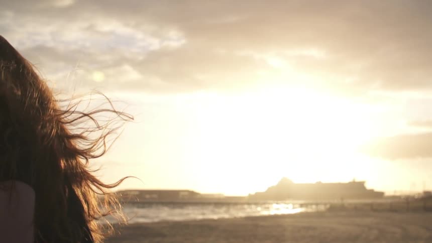 Woman walks on the beach as her hair blows in the wind