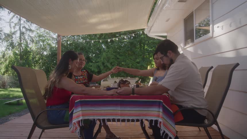 Hispanic family gathered at the table praying before thier meal outdoors on the patio
