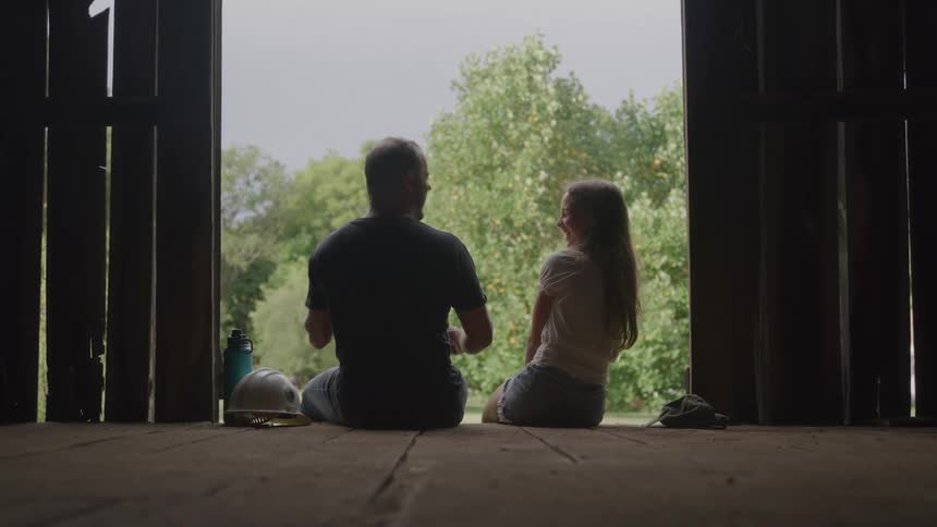 A father is talking with his daughter while sitting in the barn