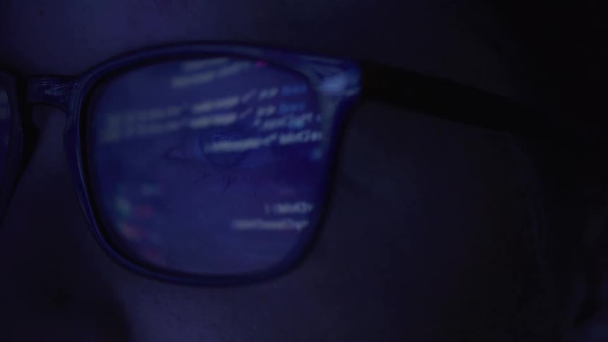 Reflection of code lines appears on persons glasses in a dark setting