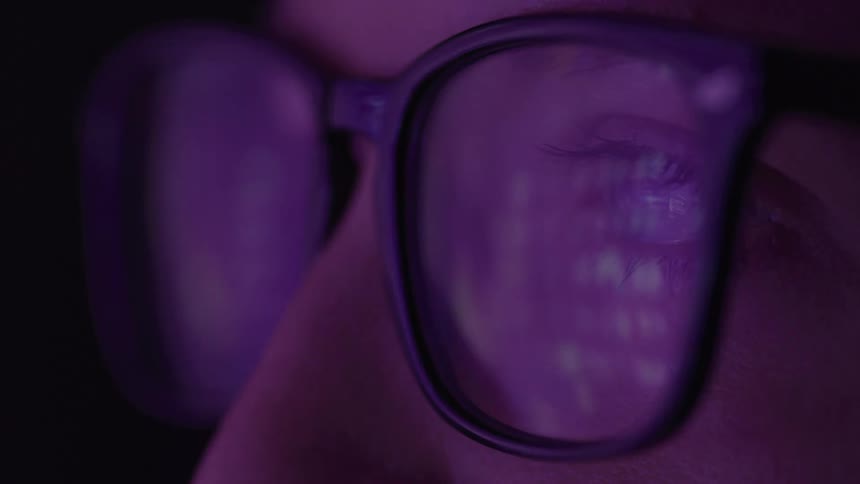 Eye reflected in eyeglass lens under purple lighting