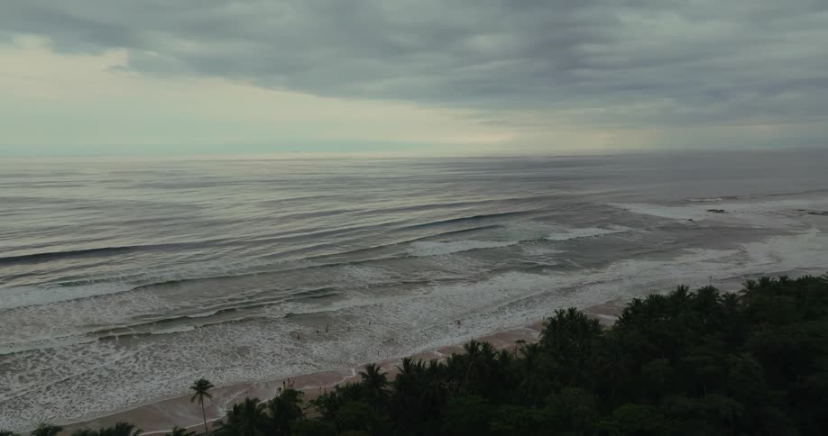 Strong waves crash onto the beach under a cloudy sky