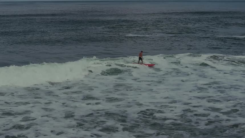 Surfer standing on red board rides a small wave