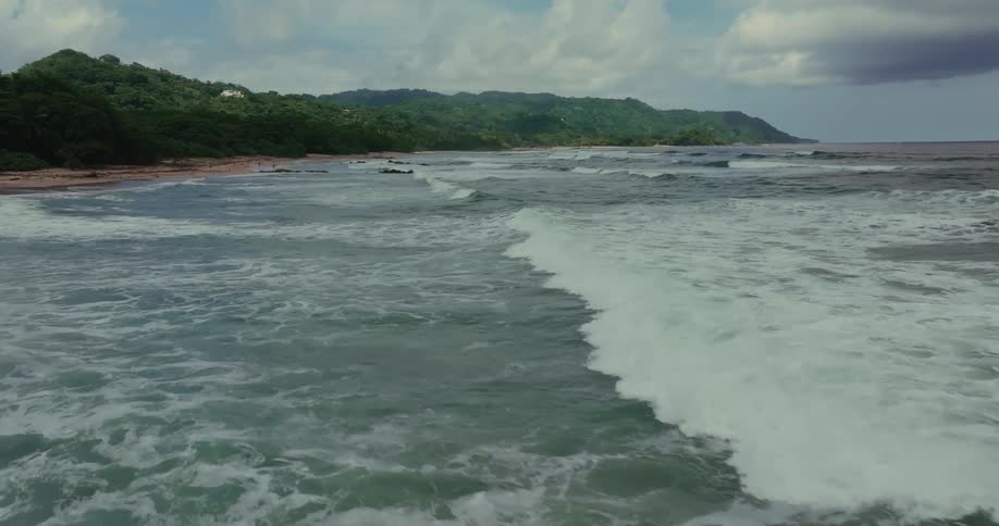 Waves approach the beach surrounded by green hills under a blue sky