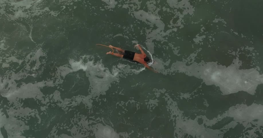 Overhead view of a surfer paddling through the waves in the ocean