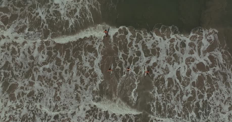 Small group of male surfers carrying surf boards walking from a beach into the sea outdoors