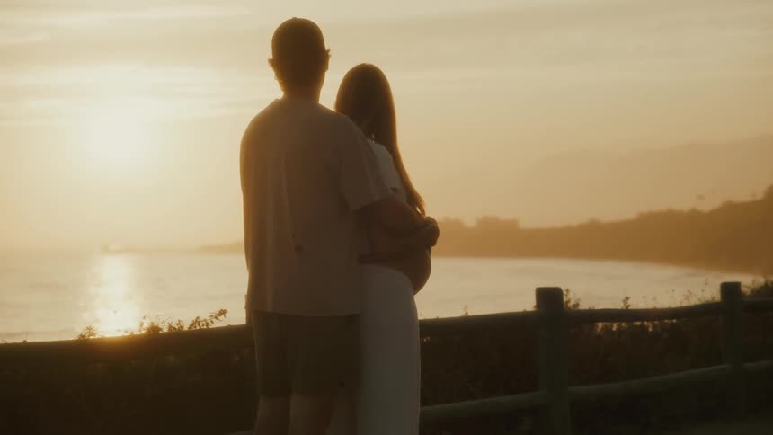 Couple embraces facing the sea during sunset