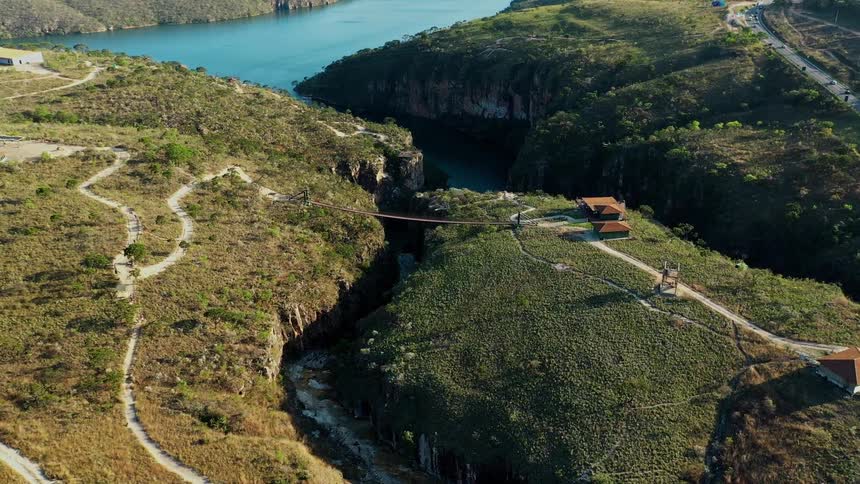 Two buildings on a highland by the shore with a bridge linking two hills and a nearby lake at midday