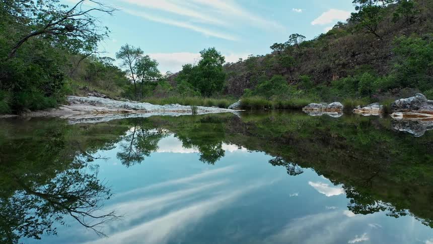 Calm river reflects clouds and trees surrounded by hills