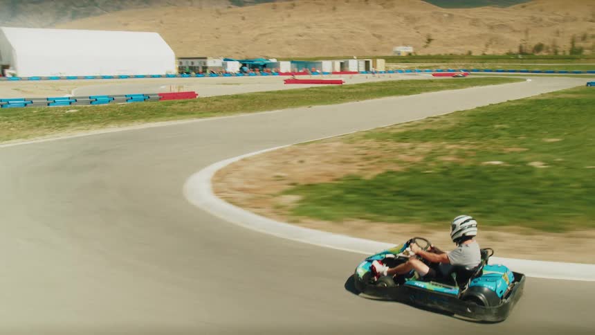 Man steers a race kart around a track located near the mountains while racing with others