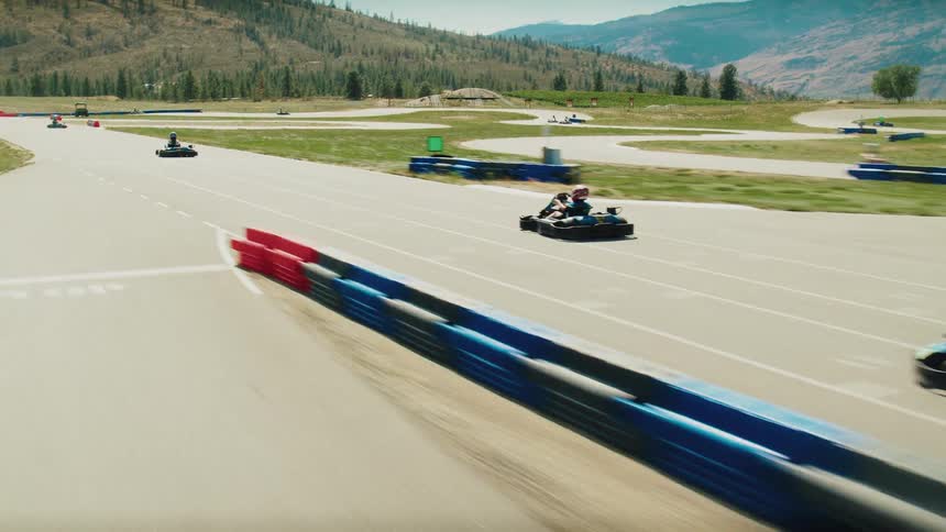 A group of people is racing on a gokart track surrounded by mountains and a natural landscape the video shows them speeding along the paved track and navigating the curves