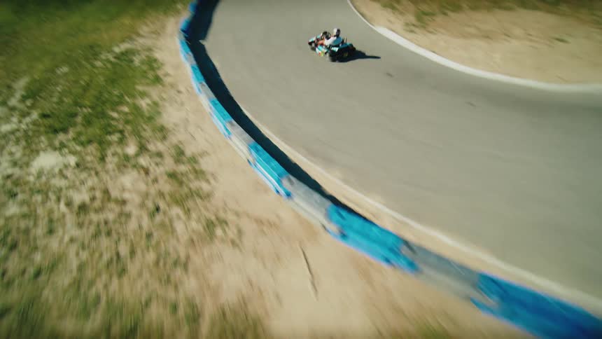 A go kart with two people in it races around a track with a view from the back as it passes other go karts