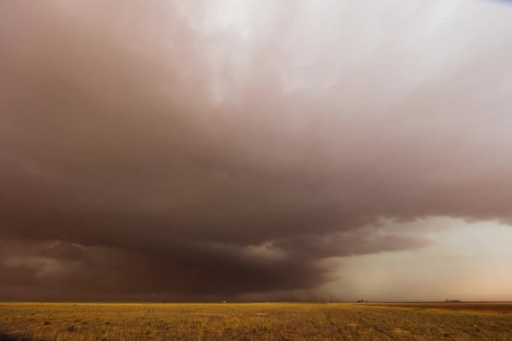 The video shows a developing tornado with a large ominous cloud funnel descending toward the ground the storm hovers over an open field with a vast gray sky above