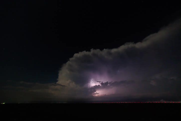 A dark night sky is illuminated by lightning striking in the distance the flashes of light reveal a massive storm cloud hovering over a dark horizon