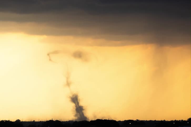 The video shows a timelapse of a tornado forming and dissipating the thin twisting funnel of the tornado extends from a dark storm cloud down toward the ground where it creates a cloud of swirling dust before eventually fading away