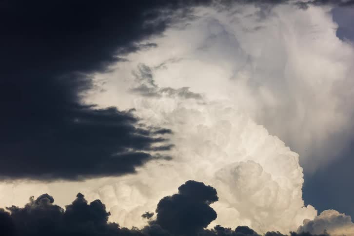 The video shows a timelapse of a massive white cumulonimbus cloud growing and dominating the sky over the course of the clip dark ominous clouds encroach from the left eventually covering the brighter clouds