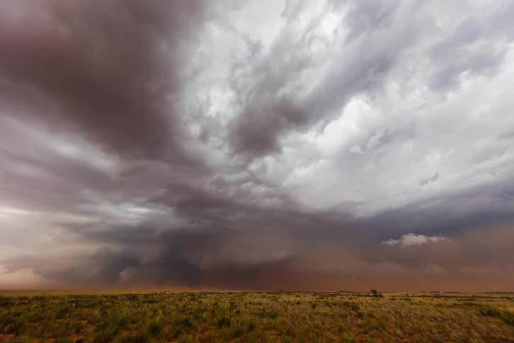Dark storm clouds loom over the open plain under a dramatic sky