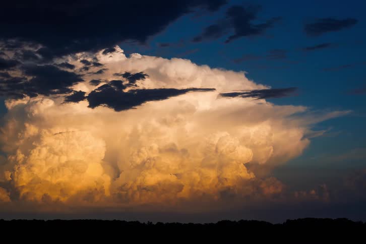 A dramatic timelapse captures a massive storm cloud billowing over the horizon its core glowing with the golden light of sunset