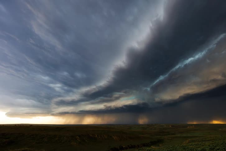 A massive thunderstorm rolls across open plains under a dramatic sky